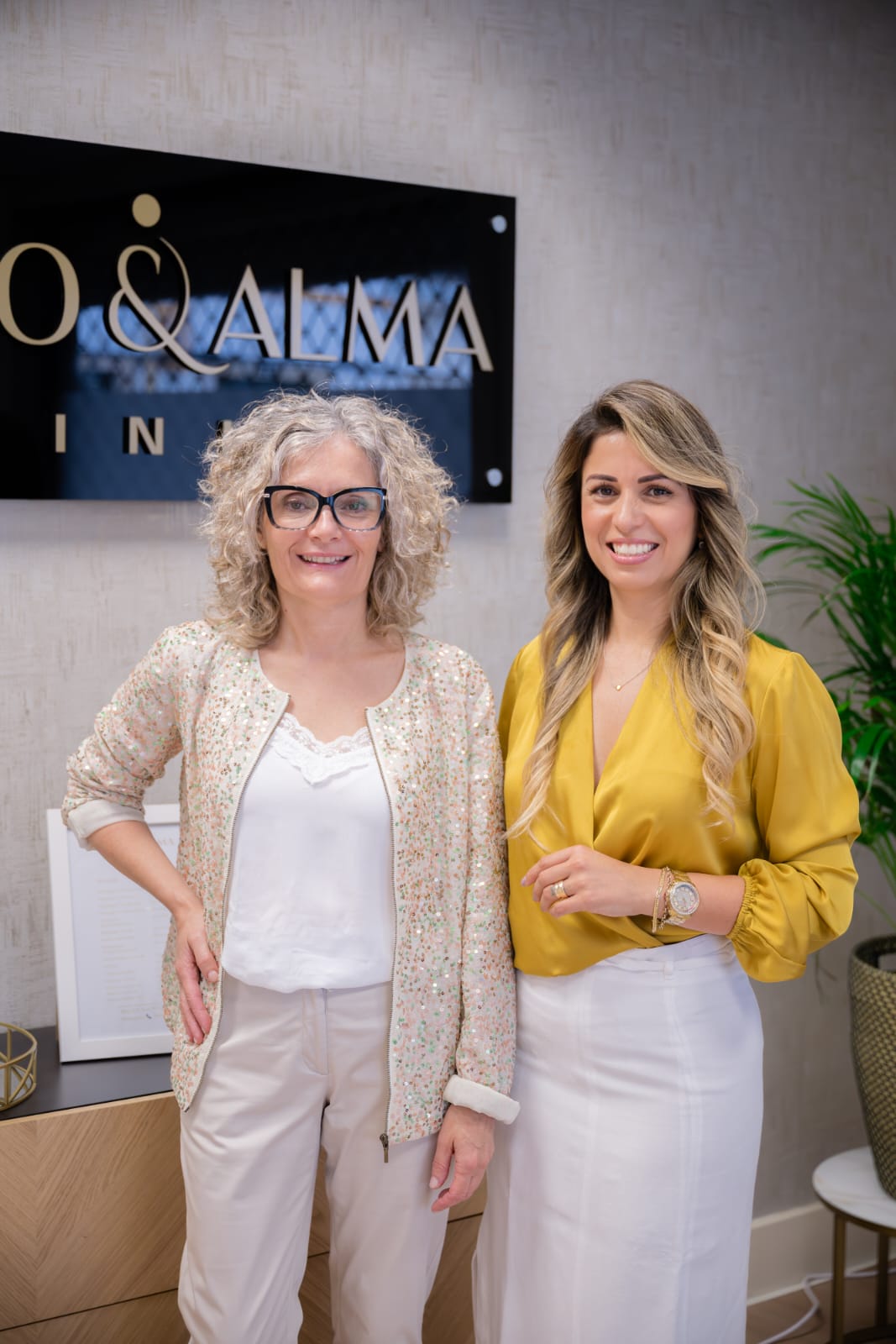 Jana Souza e Gi Miranda, fundadoras e terapeutas da Corpo & Alma Clinic, junto à placa da marca