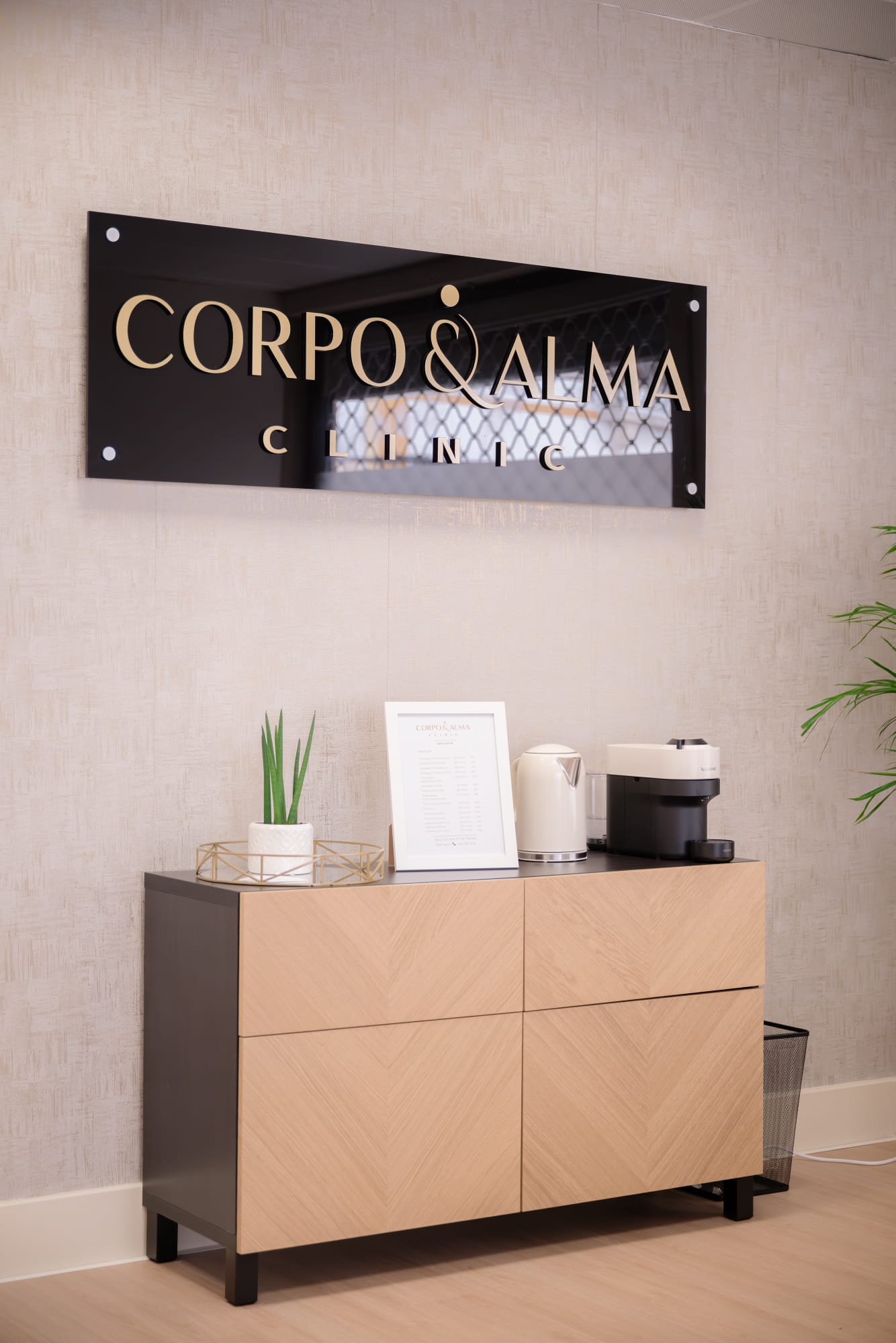 Receção da Corpo & Alma Clinic em Tomar, com placa da marca em dourado, aparador claro e plantas